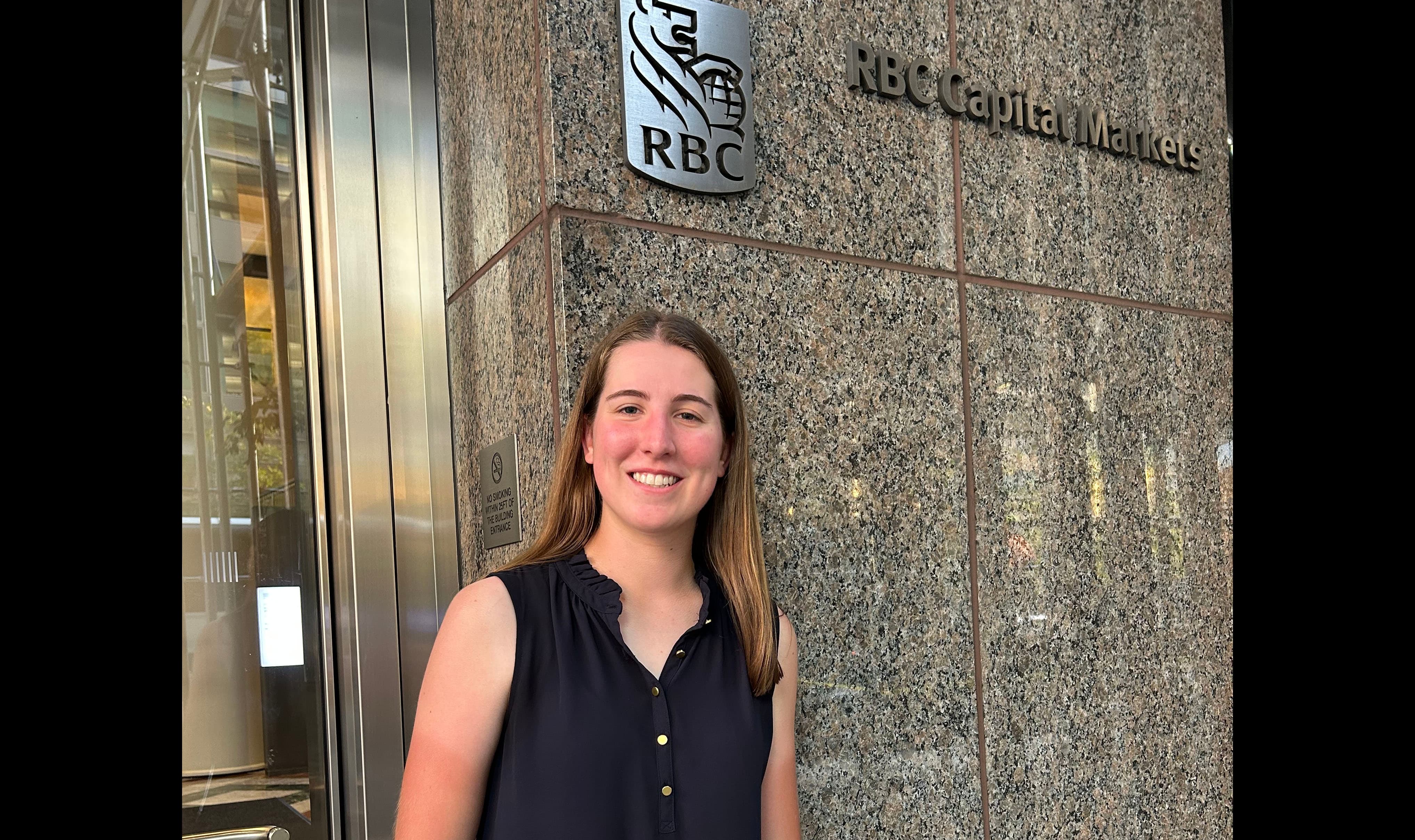 young woman standing in front of a glass door and marble wall that features the logo RBC and the words RBC Capital Markets