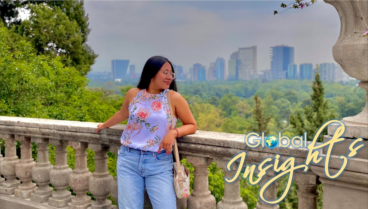 Hispanic female in light blue top standing in front of a Mexico city skyline. 
