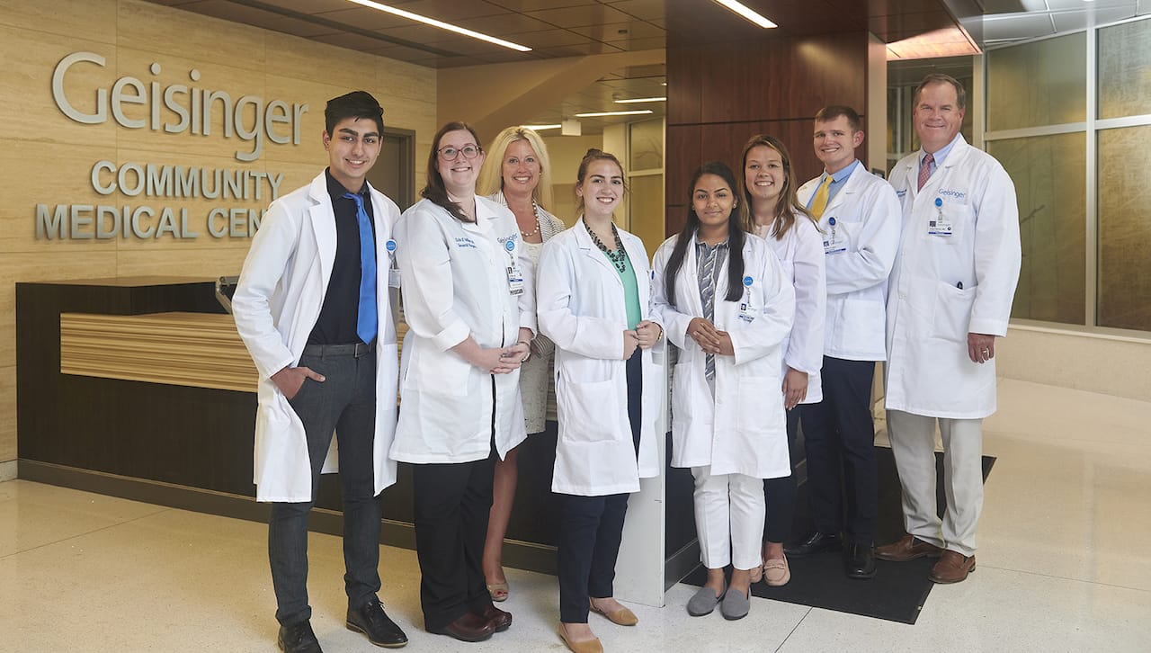 Five area college students are gaining clinical exposure and an inside look at medical school thanks to a new program at was designed to increase the chances for talented local students to gain acceptance to medical school and to remain in the region to care for their neighbors. Seen from left are Mahad Muhammad, University of Scranton student; Geisinger surgeon, Erin Miller, DO; program founder, Michelle Schmude, Ed.D., GCSOM’s associate dean for admissions, enrollment management and financial aid and associate professor; Christina Carachilo, University of Scranton student; Parita Ray, University of Scranton student; Katherine (Kate) Musto, University of Scranton student; Michael Kovalick, Wilkes University student; and program founder and University of Scranton alumnus, Joseph Bannon, MD, a Geisinger surgeon and clinical faculty member at GCSOM.