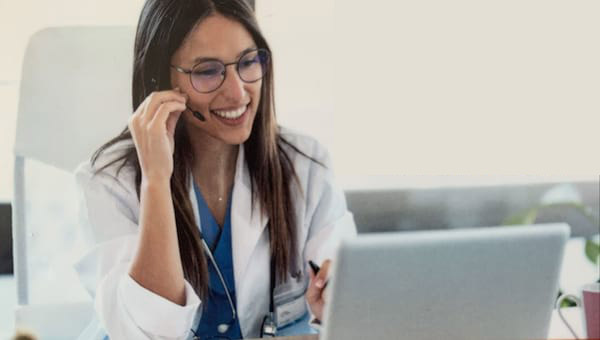 Image of SwiftMD card featuring woman wearing a white coat, speaking into a headset and using a laptop computer.