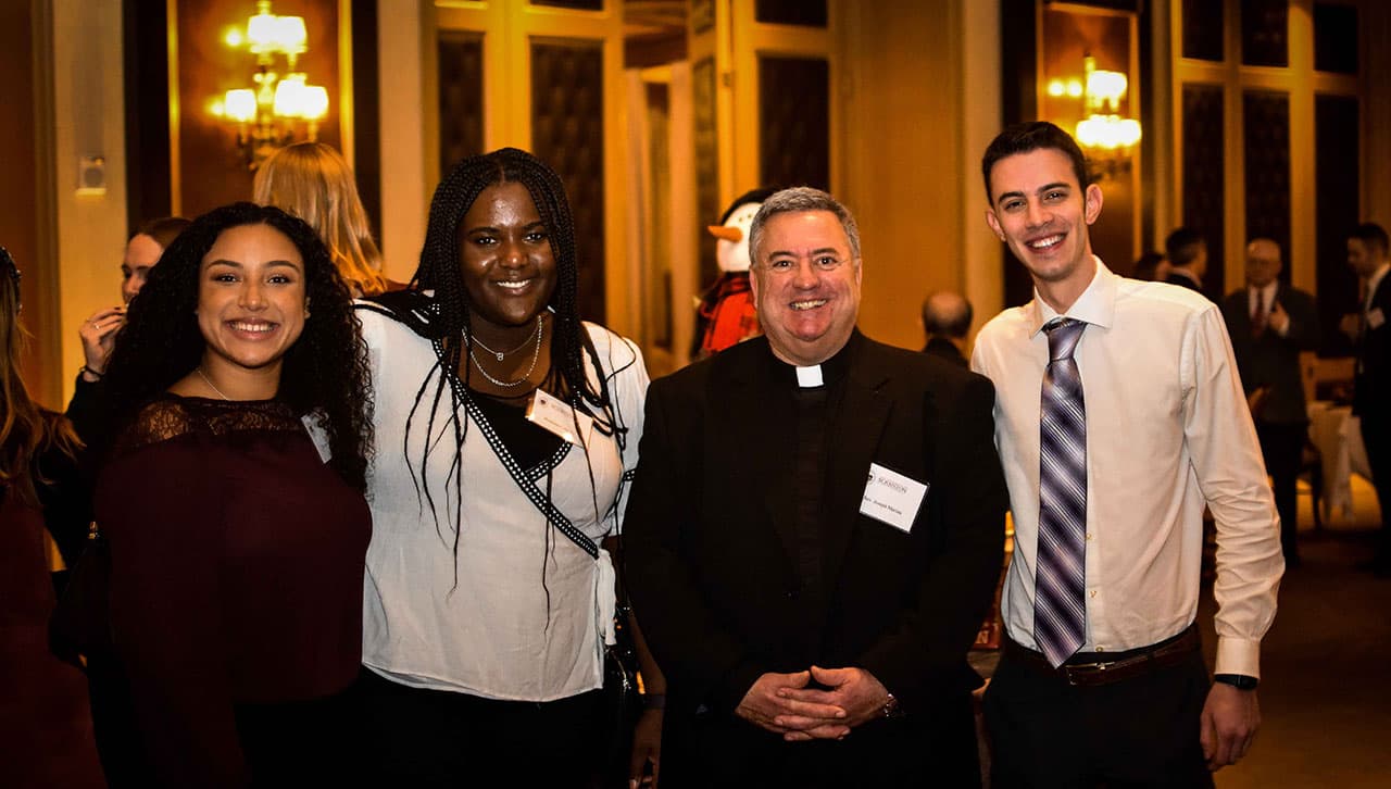 From left, Taylor Roman '21, Breanna Cole '21, Rev. Joseph G. Marina, S.J., University president, and Jeffrey Colucci '21 enjoy a moment together at the 2021 NYC Presidential Christmas Party at The New York Athletic Club. 