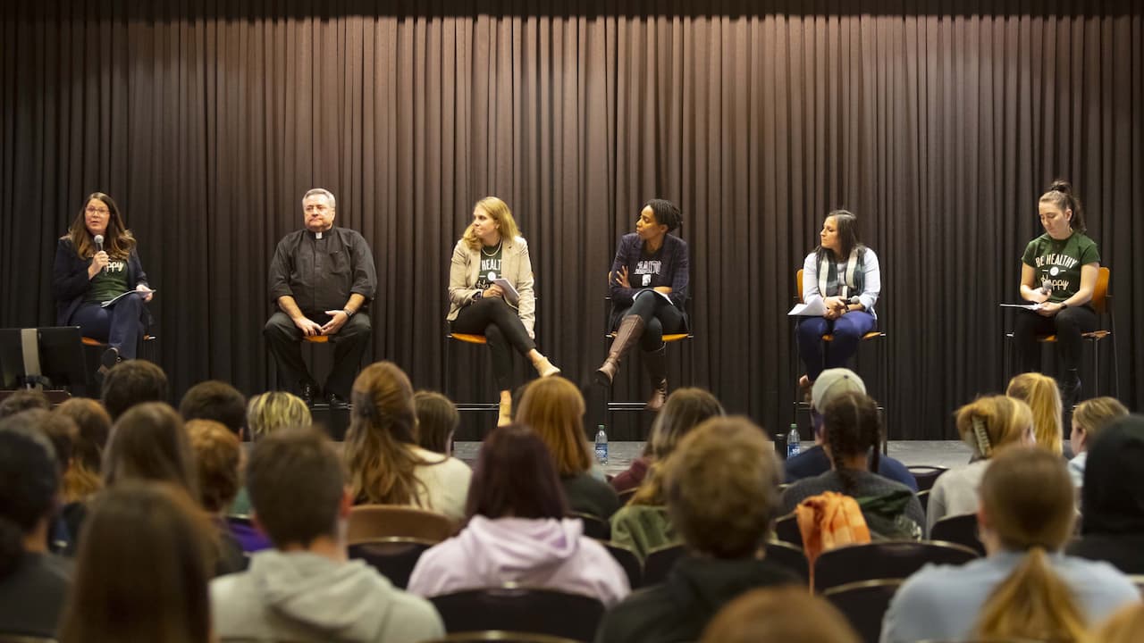 people seated on stools on a stage as part of a panel