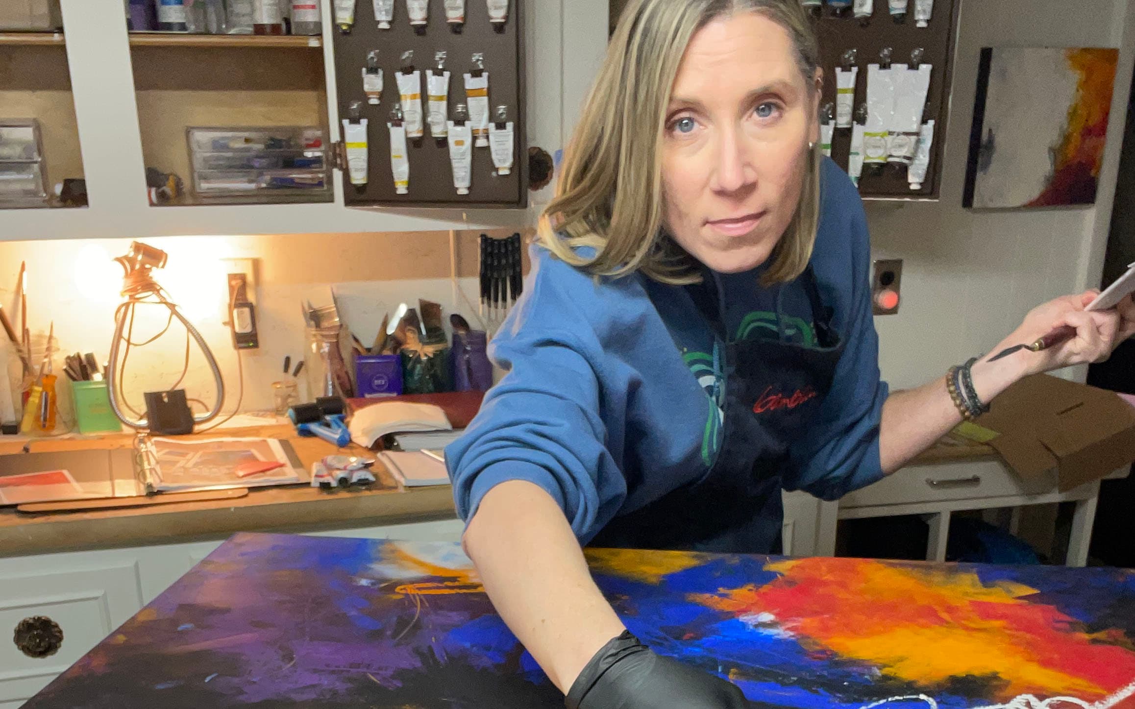 woman in an art studio with a brightly-colored painting on a table in front of her 