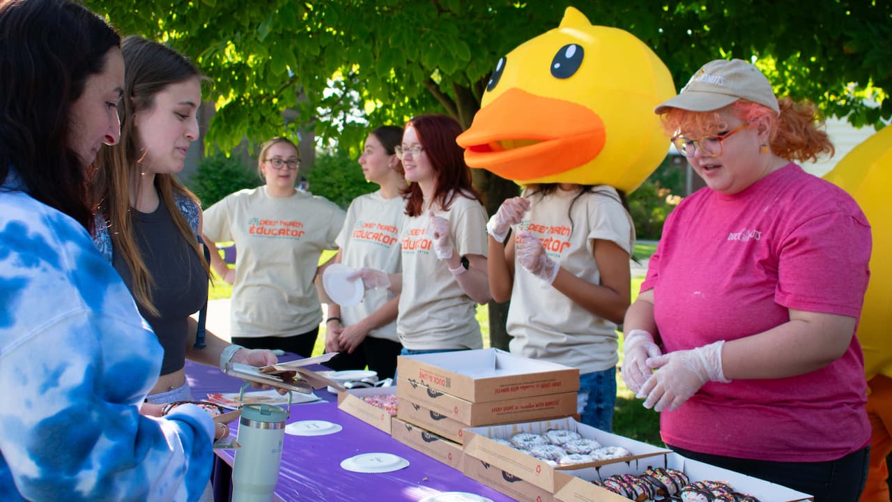 Sarah Baker '25, a Peer Health Educator Leader with CHEW invites students to attend a Be Happy Hour on Sept. 27.Shown, Peer Health Educators offer Duck Donuts to attendees at a Be Happy Hour hosted earlier in September.