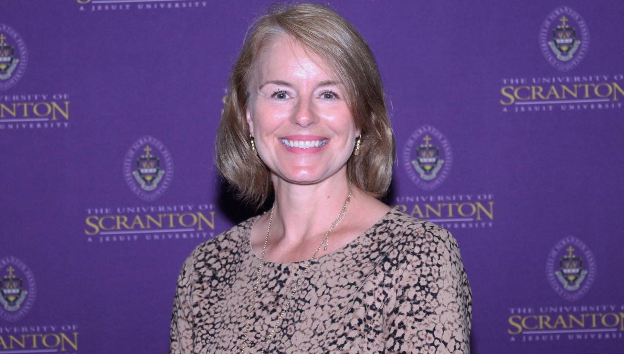 a smiling professor in front of a university of scranton-branded backdrop