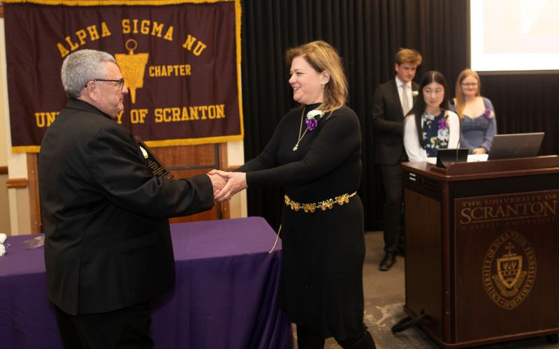 two individuals shake hands as an award is presented