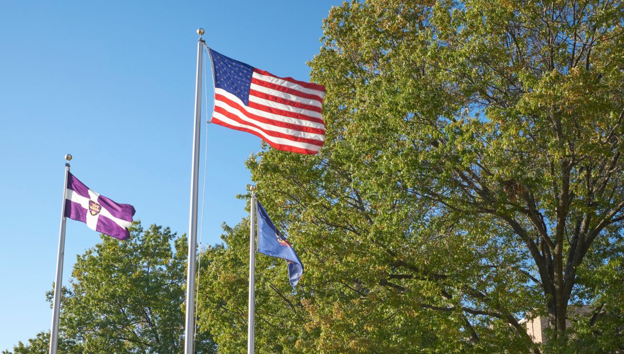 the red, white and blue united states flag flies with other flags on a flagpole