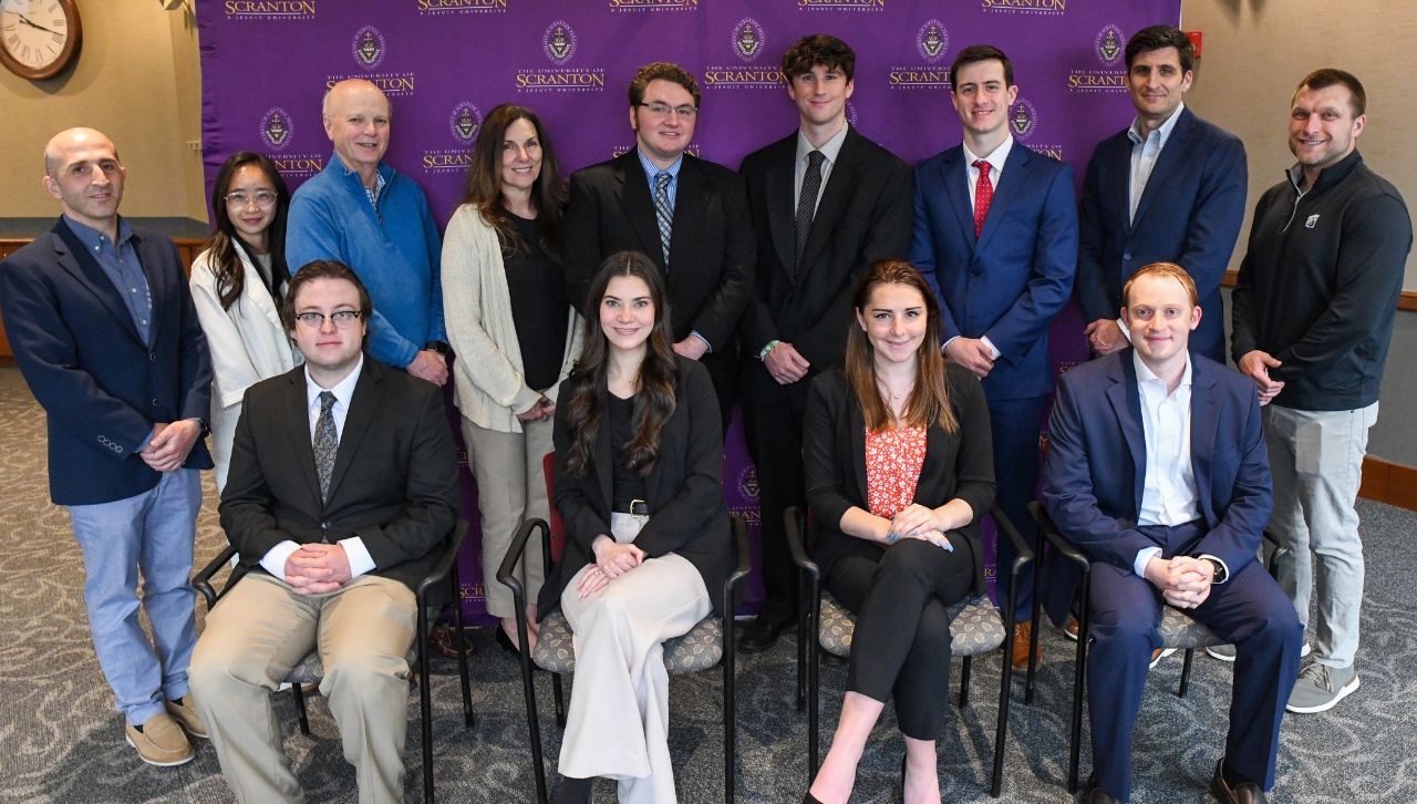 individuals, some standing and others seating, smile and pose for a picture indoors