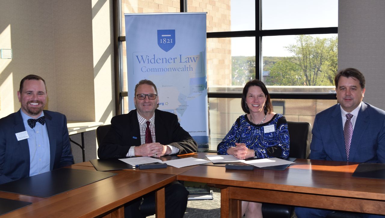 Group of professionals sitting at a conference table with a "Widener Law Commonwealth" banner in the background.