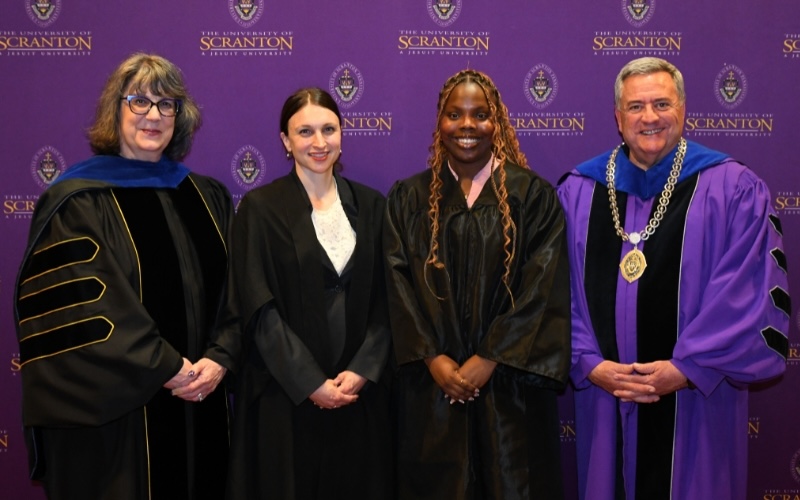 four individual stand, in front of a purple university of scranton backdrop, smiling for a picture