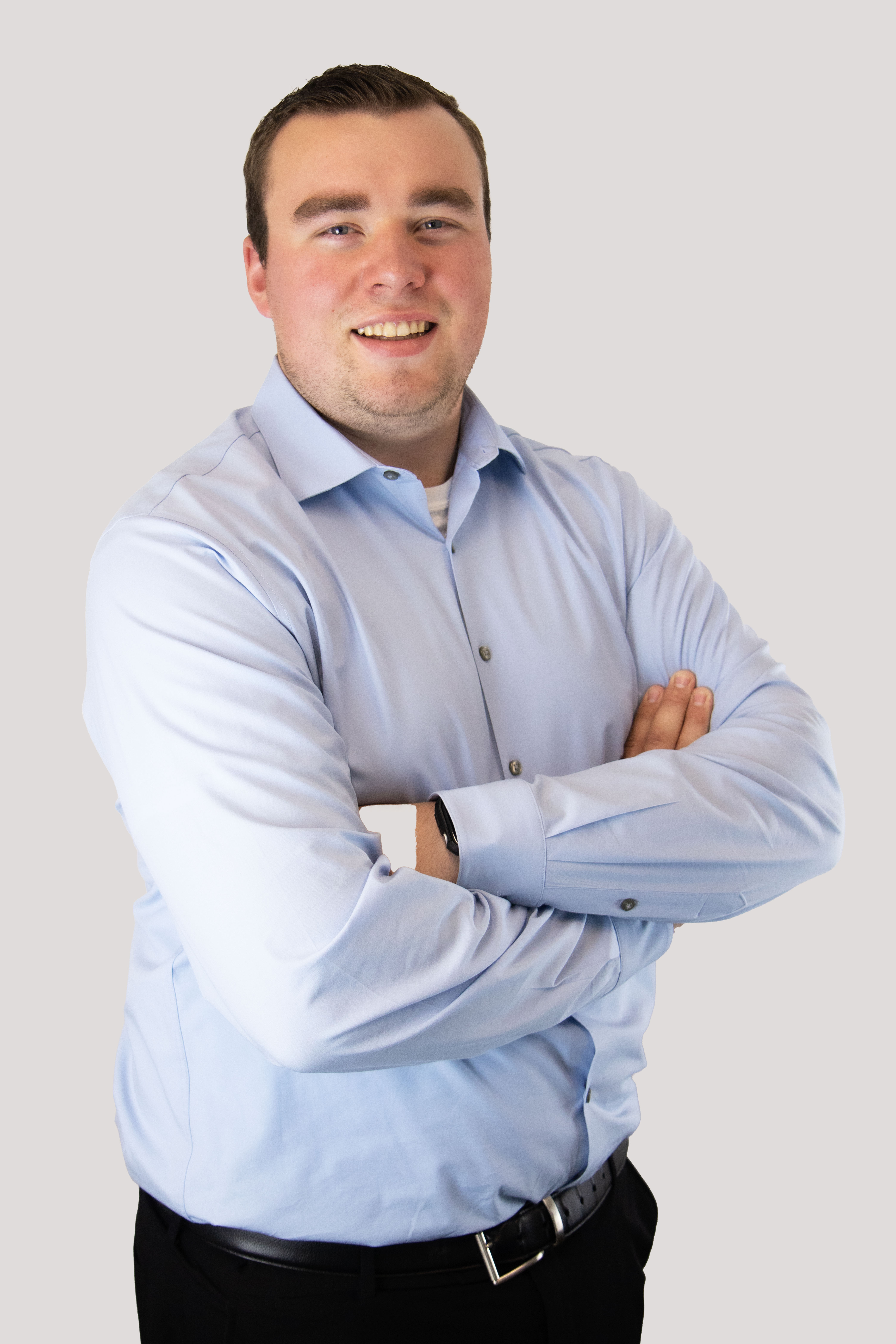 Professional headshot of a smiling man in a light blue dress shirt with arms crossed.