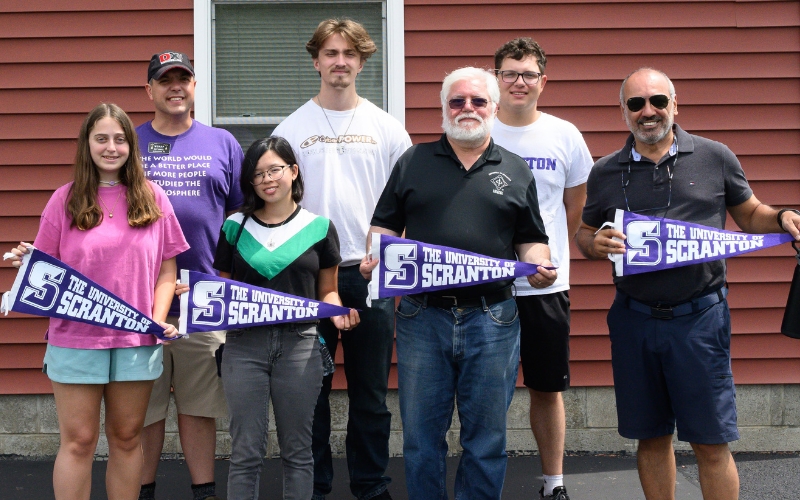 Group of students and faculty holding banners from The University of Scranton, posing in front of a building.
