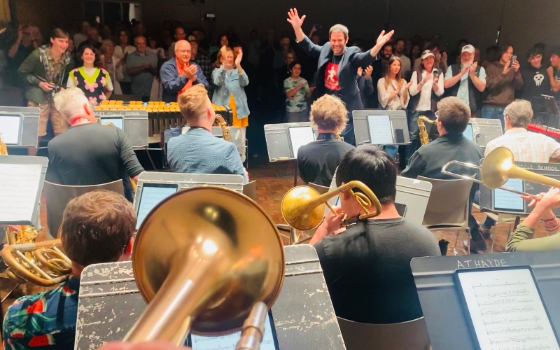 A lively band performance with musicians enthusiastically playing instruments while a cheering audience applauds in the background.
