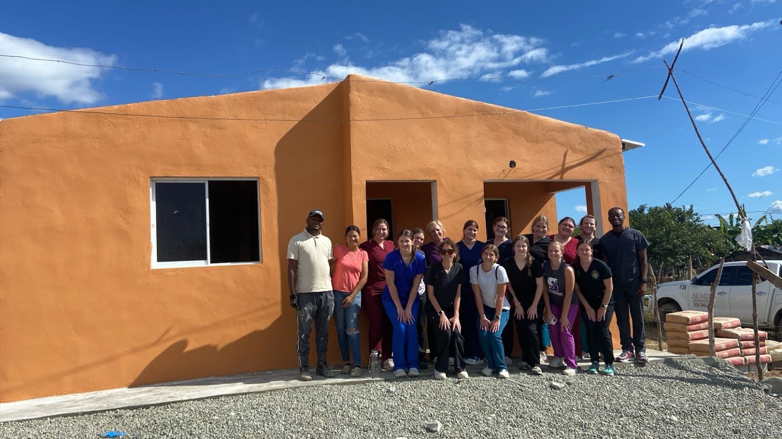 The group of fourteen University of Scranton occupational therapy students and their faculty leader stand with the recipients of the finished house build in San Juan de la Maguana, Dominican Republic.