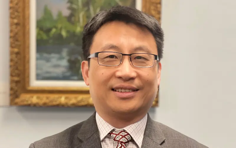 Smiling individual in a suit and glasses.